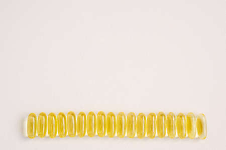 Soft gel capsules lie in a row. Vitamin D3 supplementation, group of pills on a neutral pink background with copy space for text.の写真素材