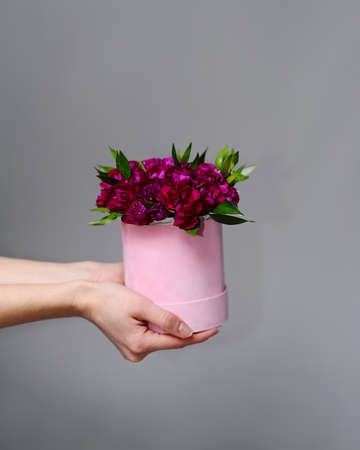 Round flower composition of pink flowers in cylindrical gift box. Red roses, flat lay. Bright fuchsia bouquet on gray background. Valentines day present.の写真素材