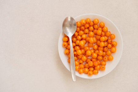 Organic sea buckthorn in a white plate. Layout on a gray table, flat lay. Fresh orange berries in...