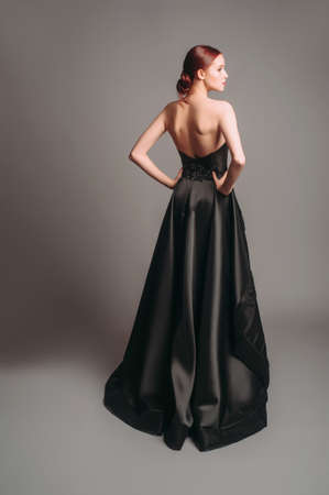 Black ball gown. Attractive ginger young woman in sleeveless evening dress on studio background. Holiday outfit. A line backless dress. Dramatic look.の写真素材
