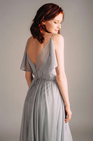 Beautiful young woman in dust blue dress. Studio portrait of ginger lady in evening gown dancing on high heel shoes in studio. Bridesmaid's outfit for hen party, rear view.の写真素材