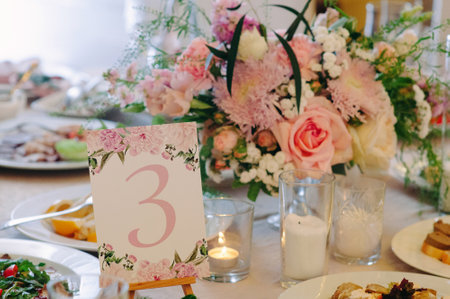 Elegant table setting for wedding reception close-up. Festive bouquet with fresh tender pink flowers, candles and cards on dining table at restaurantの写真素材