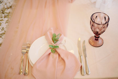 Romantic table decoration in blush pink. Floral decor and napkin on plate, wineglass and cutlery top view. Elegant table settingの写真素材
