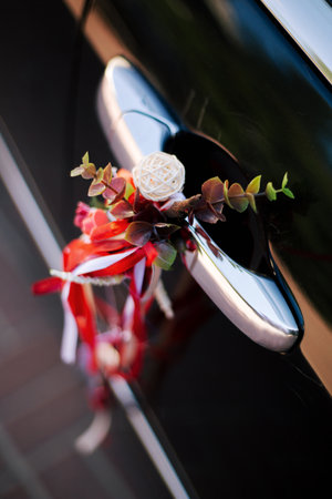 Door handle of black bridal car decorated with flowers and ribbons for holiday. Wedding details close-up in white and redの写真素材