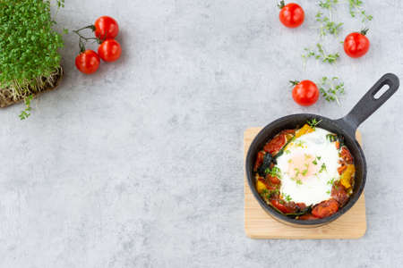 Baked egg with vegetables: tomatoes, bell peppers, spinach and garden cress. Shakshuka in a skillet on gray background.の写真素材