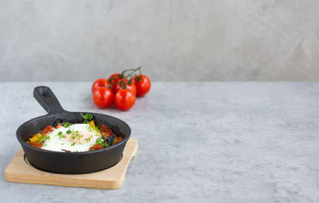 Baked egg with vegetables in a skillet sprinkled with garden cress. Healthy breakfast with eggs, tomatoes, bell pepper, spinach and microgreens on gray background. Copy space.の写真素材