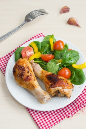 Two roasted chicken legs with salad from spinach, cherry tomatoes and bell pepperの写真素材