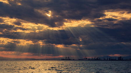 Bright cloudy sunset at the seaside overlooking silhouettes of the cranes in the industrial part of...