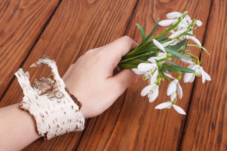 Snowdrops in a female hand with a bracelet on a birchの写真素材