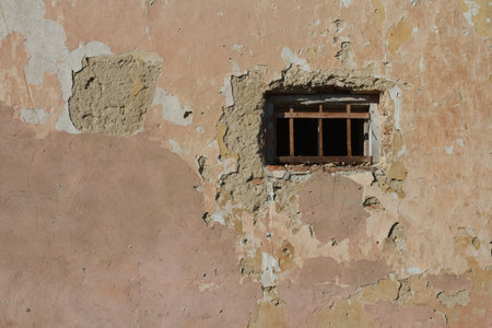 old small window with bars in a wall covered with plaster
