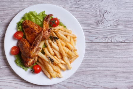 Two fried chicken wings, french fries, tomato and lettuce on a plate. top view
の写真素材
