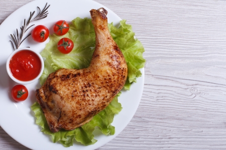 Roasted chicken leg with rosemary, lettuce and tomato on a white plate. top view
の写真素材