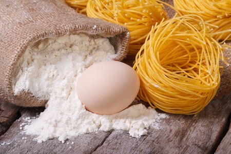 dry pasta in the form of nests, a raw egg and a bag of flour close up on an old wooden table. macro. horizontal 
の写真素材