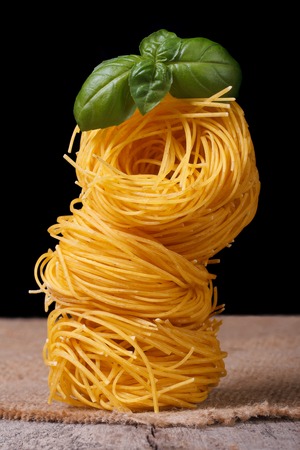 Tower of dry pasta nest closeup with green basil on the table. macro. vertical 
の写真素材