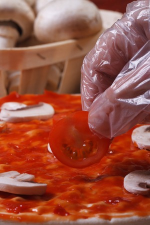 Hand in glove chef puts on a pizza base cherry tomatoes. macro. verticalの写真素材