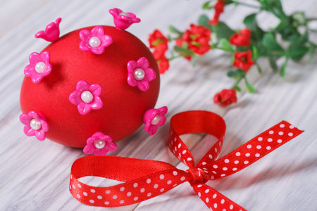 red easter egg decorated with pink flowers with bow closeup on wooden tableの写真素材