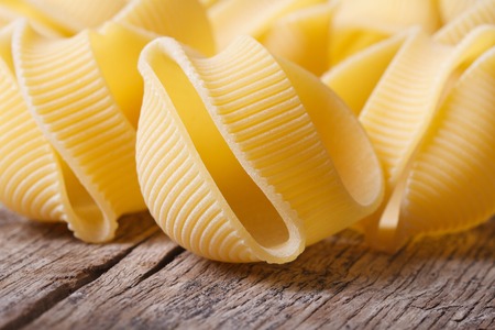 Raw Italian macaroni lumaconi scattered on the old desk closeup. horizontal 
の写真素材