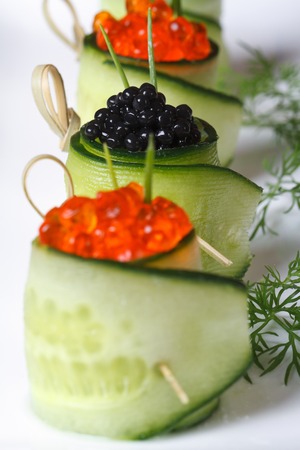 Appetizer of cucumber rolls with red and black caviar on a white plate. macro vertical
の写真素材