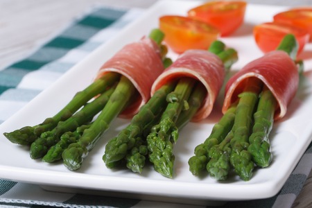 Green asparagus wrapped in ham and tomato on a white plate. close up horizontal
の写真素材