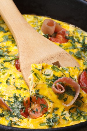 Omelette with tomatoes, ham and herbs closeup on wooden spatula. vertical 
の写真素材
