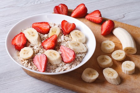 muesli with fresh strawberries and banana with chopped ingredients closeup on a wooden table. horizontal 
の写真素材