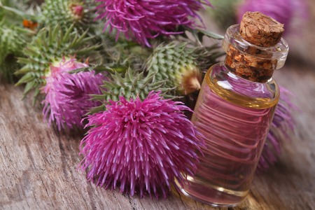 burdock oil in a glass bottle on a background of flowers. の写真素材