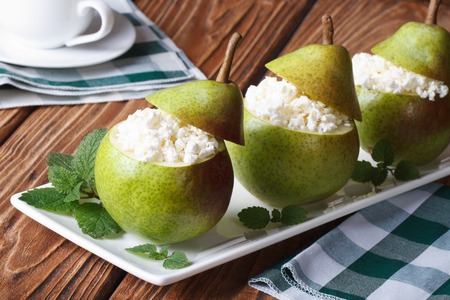 Fresh pears stuffed with cottage cheese on white plate closeup on tableの写真素材