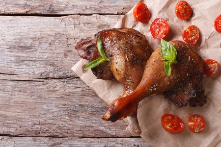 two roasted duck legs with basil and tomatoes close up on an old table top view horizontal
の写真素材