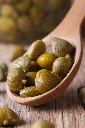ripe capers in a wooden spoon closeup on old table. verticalの写真素材