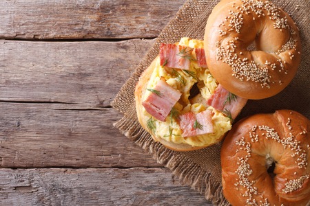 bagel with egg and bacon on an old wooden table close-up. horizontal view from aboveの写真素材