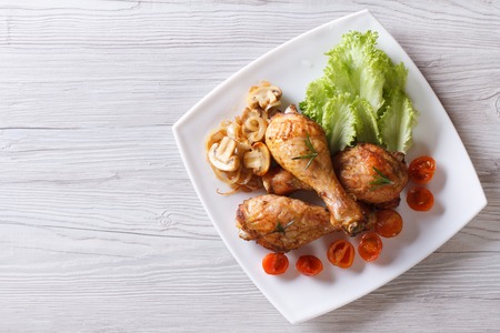 Fried chicken legs with mushrooms and tomatoes on a plate. horizontal view from aboveの写真素材