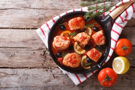 Fish in tomato sauce with olives and lemon in a frying pan. horizontal view from aboveの写真素材