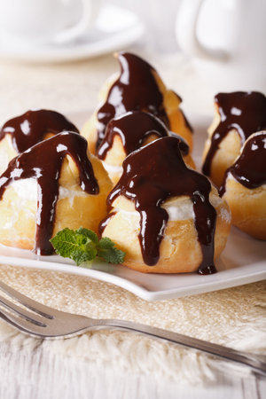 Delicious profiteroles with cream and chocolate glaze on a plate. vertical