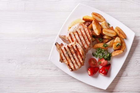 pork steak, fried potatoes and vegetables on a plate. horizontal view from aboveの写真素材