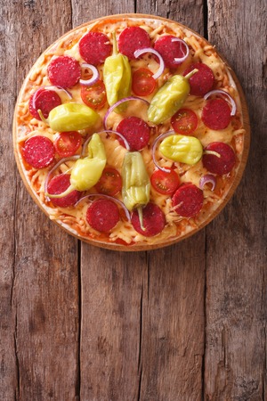 Italian pizza with salami, pepperoni pepper and tomatoes on a table close-up vertical view from above, rustic styleの写真素材