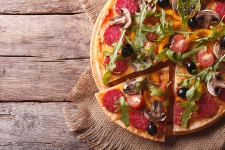 Cutting pizza with herbs, salami and vegetables close-up on the table. horizontal view from above, rustic styleの写真素材