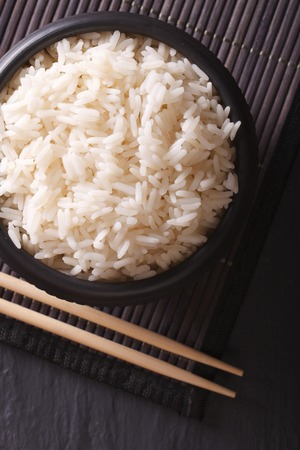 Boiled rice in a black bowl close-up and chopsticks. vertical top viewの写真素材