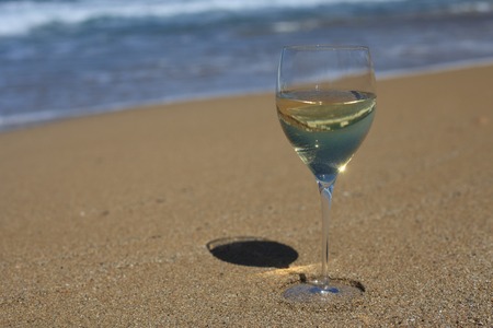 A glass of white wine in the sand on the beach closeup. Horizontalの写真素材