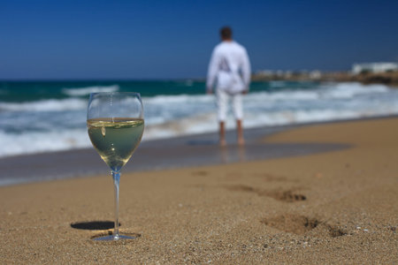 Young man near the sea and a glass of wine on the sand close-upの写真素材