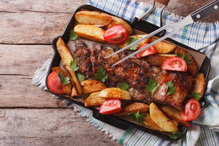 Pork ribs with baked potatoes and tomatoes in a pan close-up. horizontal view from aboveの写真素材