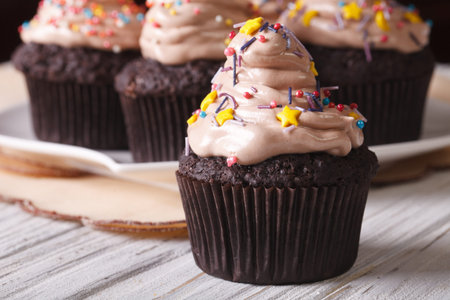Delicious chocolate cupcakes with cream and candy sprinkles on the table macro. horizontal