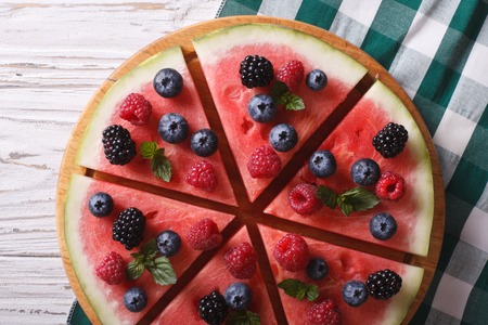 Watermelon decorated with raspberries and blueberries close-up on the table. horizontal view from aboveの写真素材