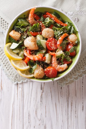 Fresh salad with seafood and vegetables in a bowl close-up on the table. vertical top viewの写真素材