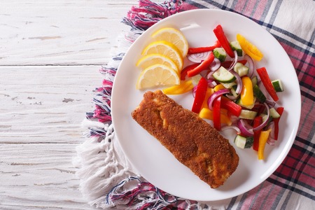 fried fish fillet with fresh vegetables and a lemon on a plate. horizontal view from aboveの写真素材