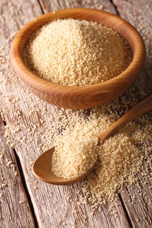 Crude Couscous in a wooden bowl and spoon on the table close-up. verticalの写真素材
