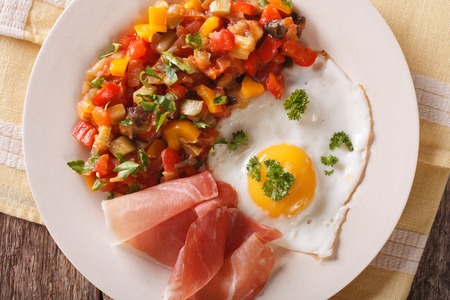 Spanish breakfast: fried egg, ham and pisto on a plate on the table. Horizontal view from aboveの写真素材