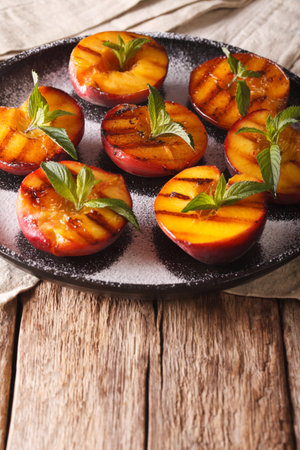 Healthy Dessert: grilled Peaches with powdered sugar and mint close-up on a plate on the table. verticalの写真素材
