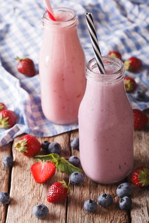Homemade milkshake with strawberries and blueberries in bottles close-up on the table. verticalの写真素材
