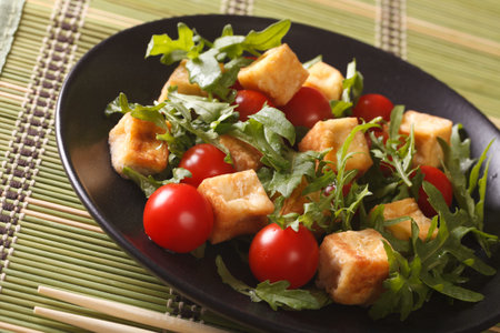 Dietary food: fried tofu with tomatoes and fresh arugula close-up on a plate on the table. Horizontalの写真素材