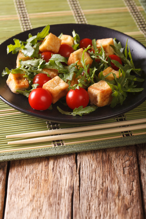 Dietary food: fried tofu with tomatoes and fresh arugula close-up on a plate on the table. verticalの写真素材